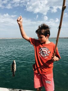 Young boy celebrates catching a fish on a sunny day by the sea.